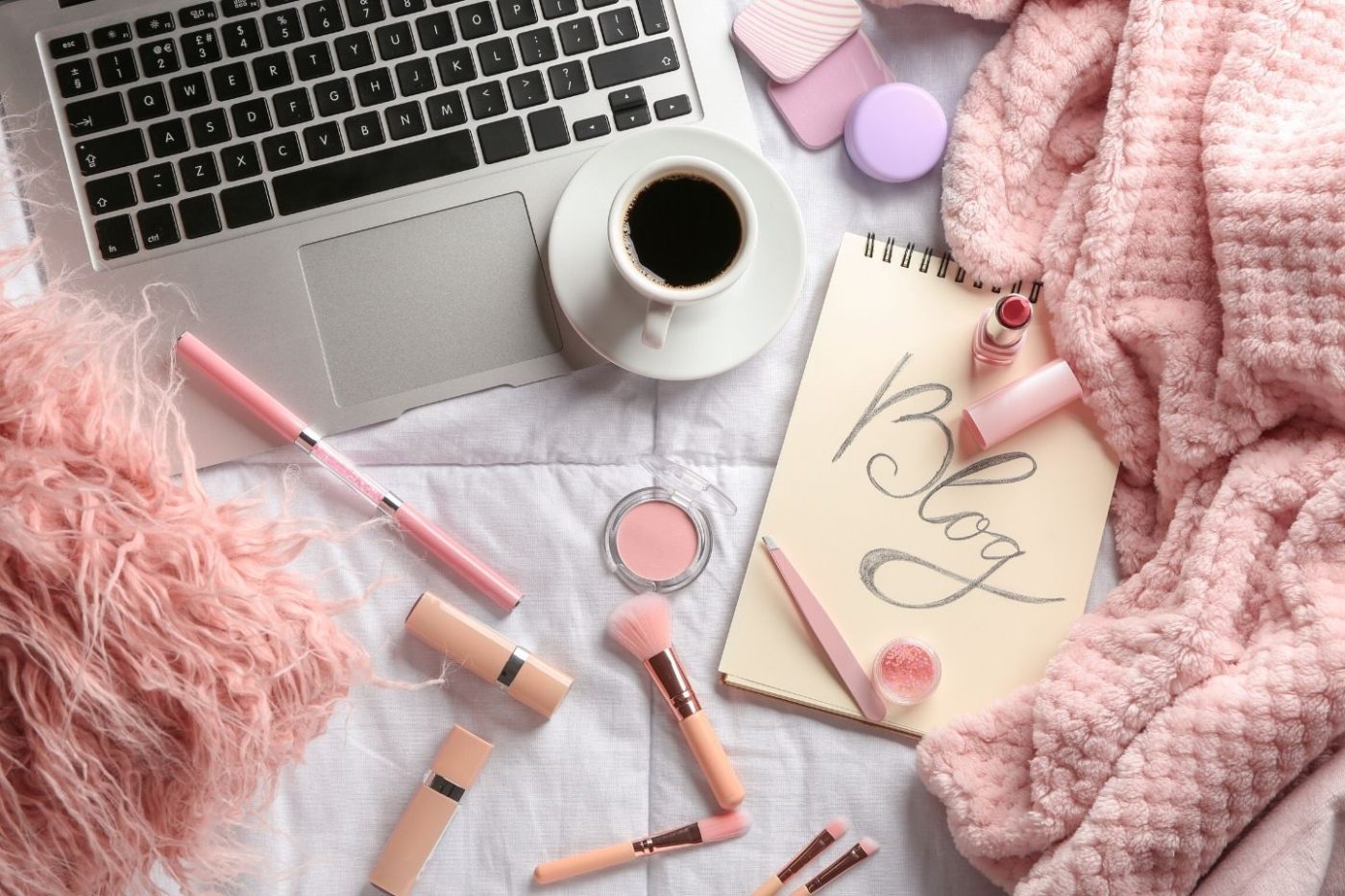 computer surrounded by makeup, coffee and a notepad that says blog