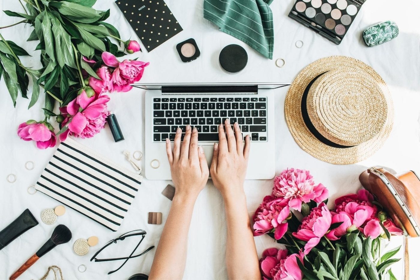 woman typing on laptop surrounded by pink flowers and fashion accessories