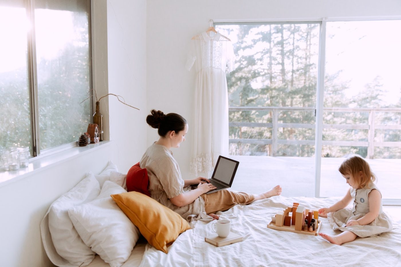 mom working on her computer while little girl plays on bed