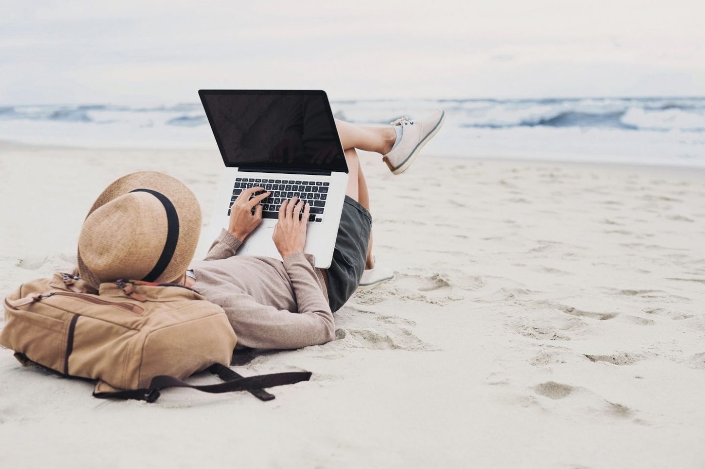 person lying on the beach working on their laptop